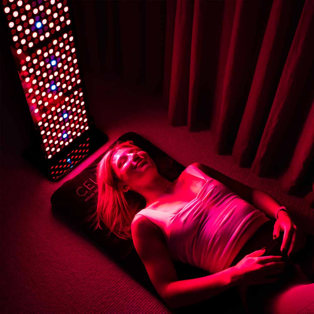 Women laying on CELLER8 PEMF mat while using CELLER8 half body red light panel