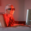 Lady using Red Light Therapy Lamp in bedroom on face